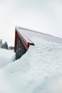 A homeowner measures roof rise from an attic using a level and tape measure beside visible rafters.