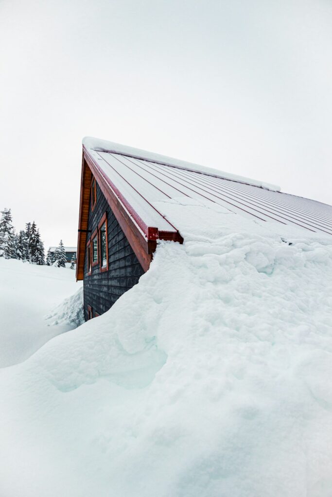 A homeowner measures roof rise from an attic using a level and tape measure beside visible rafters.